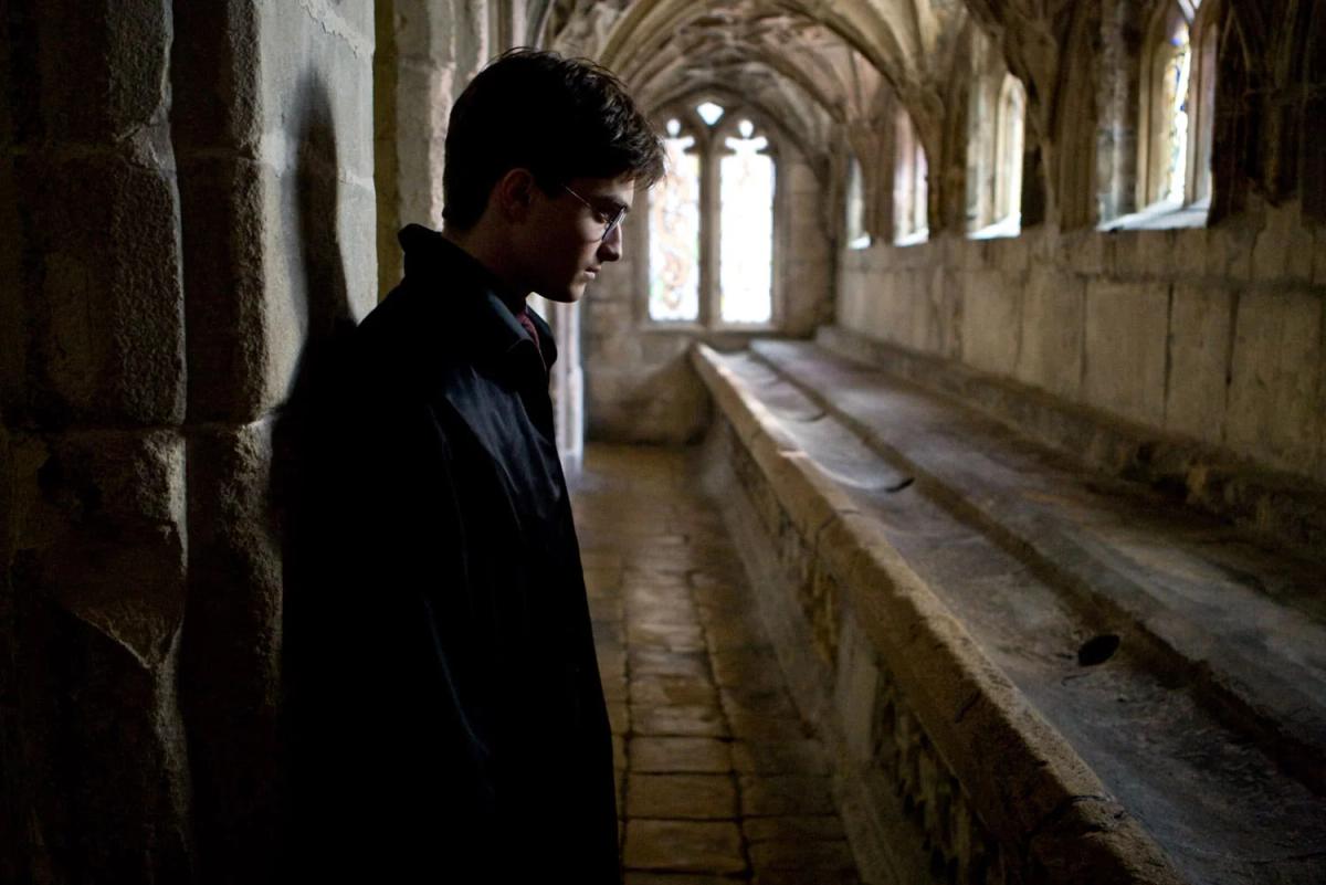 Daniel Radcliffe as Harry Potter alone in a dim stone corridor at Hogwarts