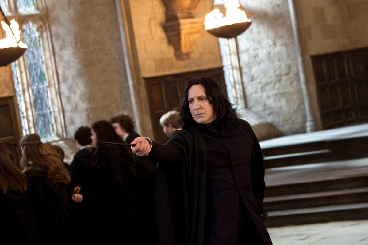 Alan Rickman as Severus Snape pointing across the Great Hall in black robes, with rows of students behind him.