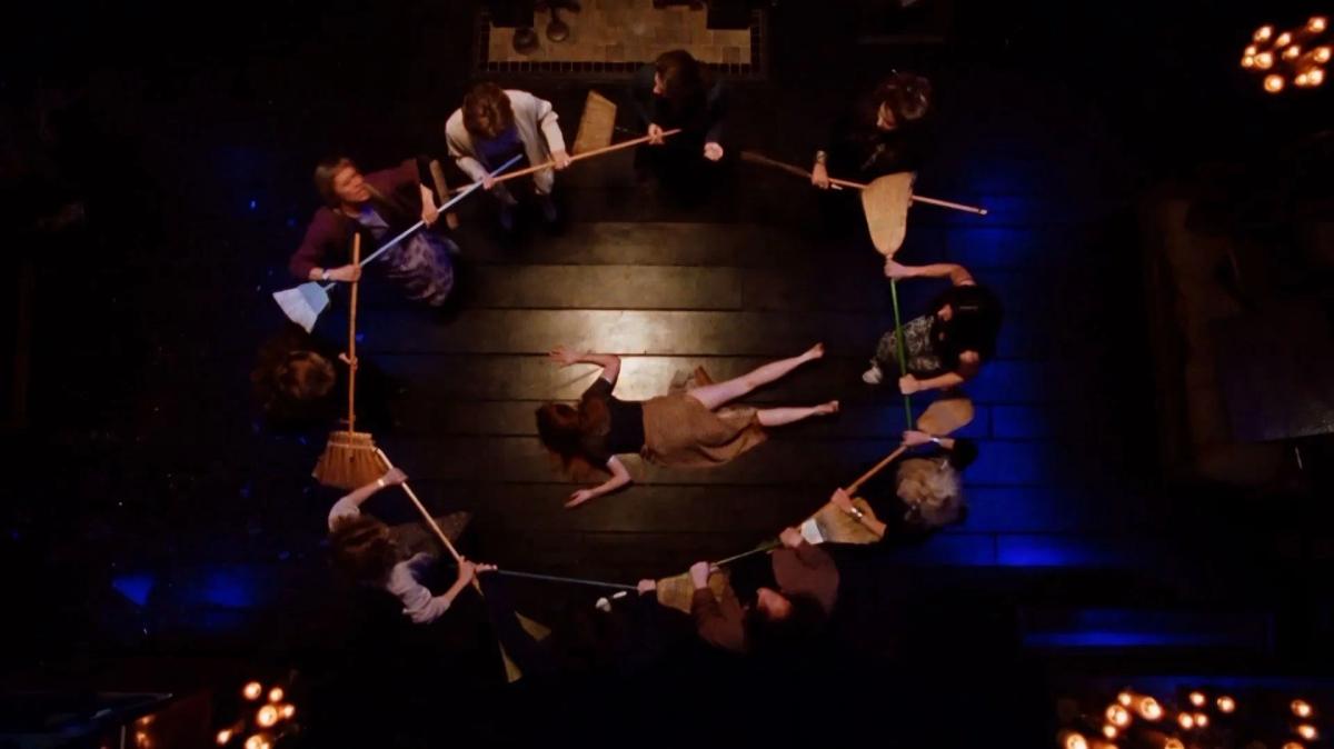 Overhead shot of the town's women standing in a circle holding brooms around Nicole Kidman as Gillian Owens, who lies on the floor.