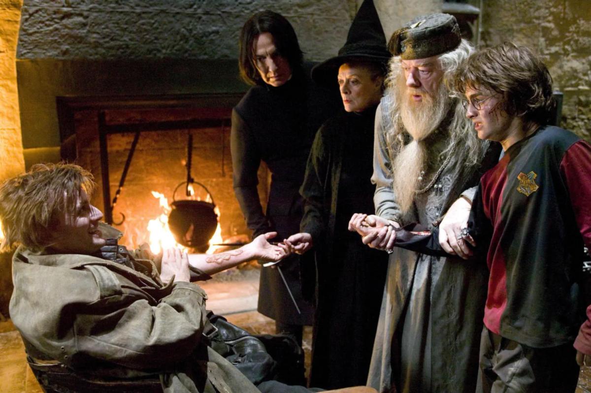 David Tennant as Barty Crouch Jr slumps by the fireplace in Moody's office as Alan Rickman as Severus Snape, Maggie Smith as Minerva McGonagall, Michael Gambon as Albus Dumbledore and Daniel Radcliffe as Harry Potter stand over him.