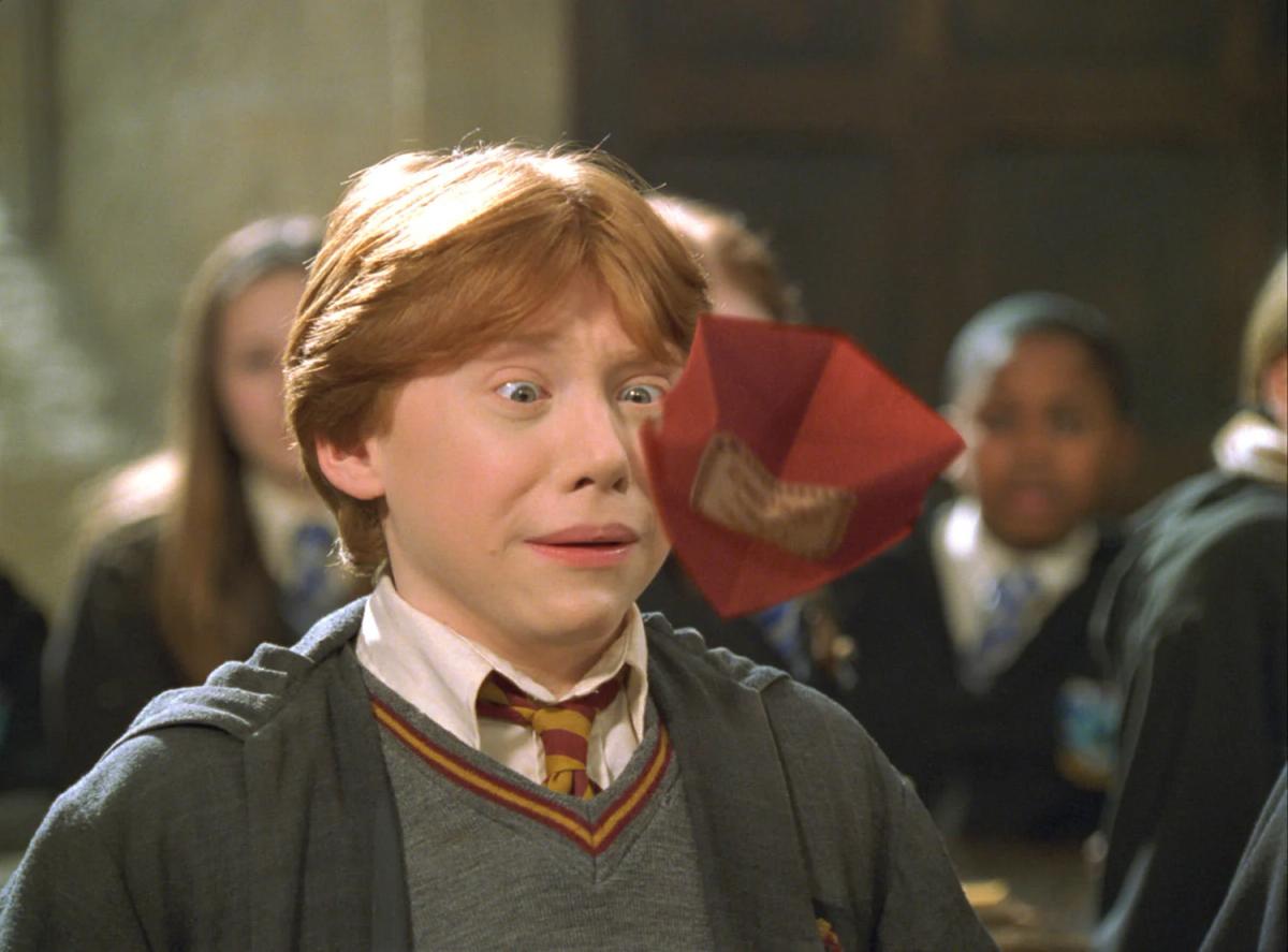 Ron Weasley (Rupert Grint) grimaces wide-eyed in the Great Hall as a red Howler envelope hovers open beside his face.