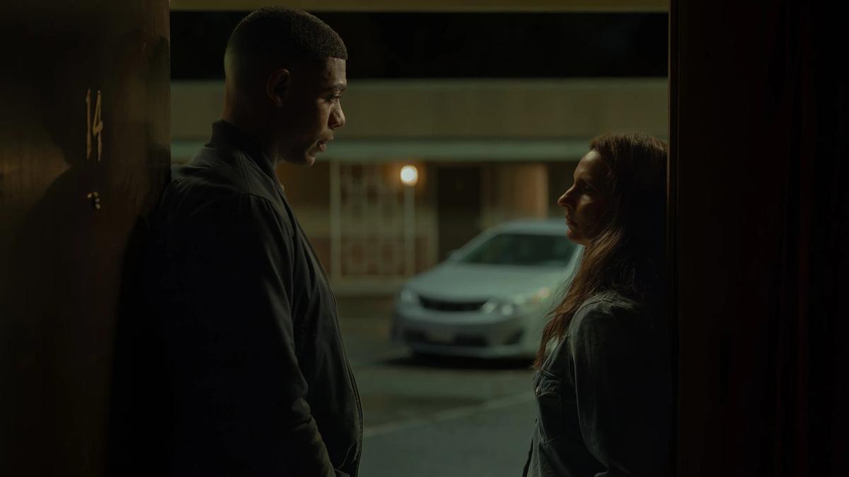 Aaron Pierre as John Stewart and Poorna Jagannathan as Zoe Macon facing each other outside a motel room at night.