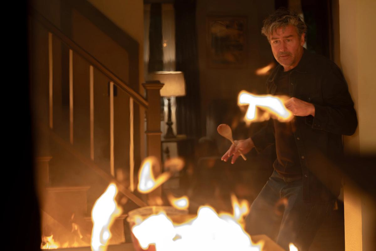 Kyle Chandler as Hal Jordan, holding a wooden spoon, backing away from flames inside his burning house.
