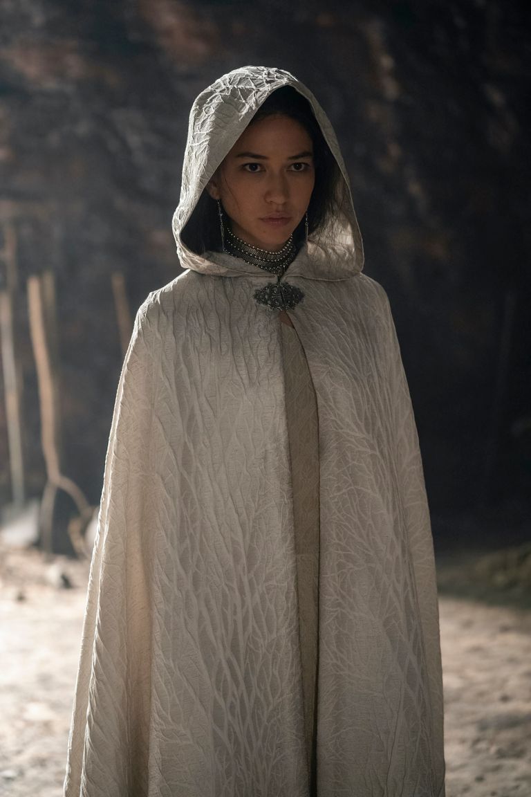 Mysaria standing alone in a pale hooded cloak, outdoors in burnt ground, looking directly ahead