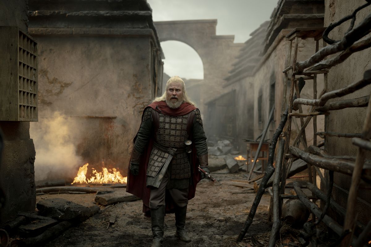 Hugh Hammer walking alone down a burnt Tumbleton street, fires still smoldering in the rubble around him