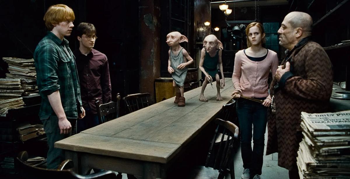 Andy Linden as Mundungus Fletcher faces Daniel Radcliffe as Harry Potter, Rupert Grint as Ron Weasley, Emma Watson as Hermione Granger, Dobby voiced by Toby Jones and Kreacher voiced by Simon McBurney at Grimmauld Place.