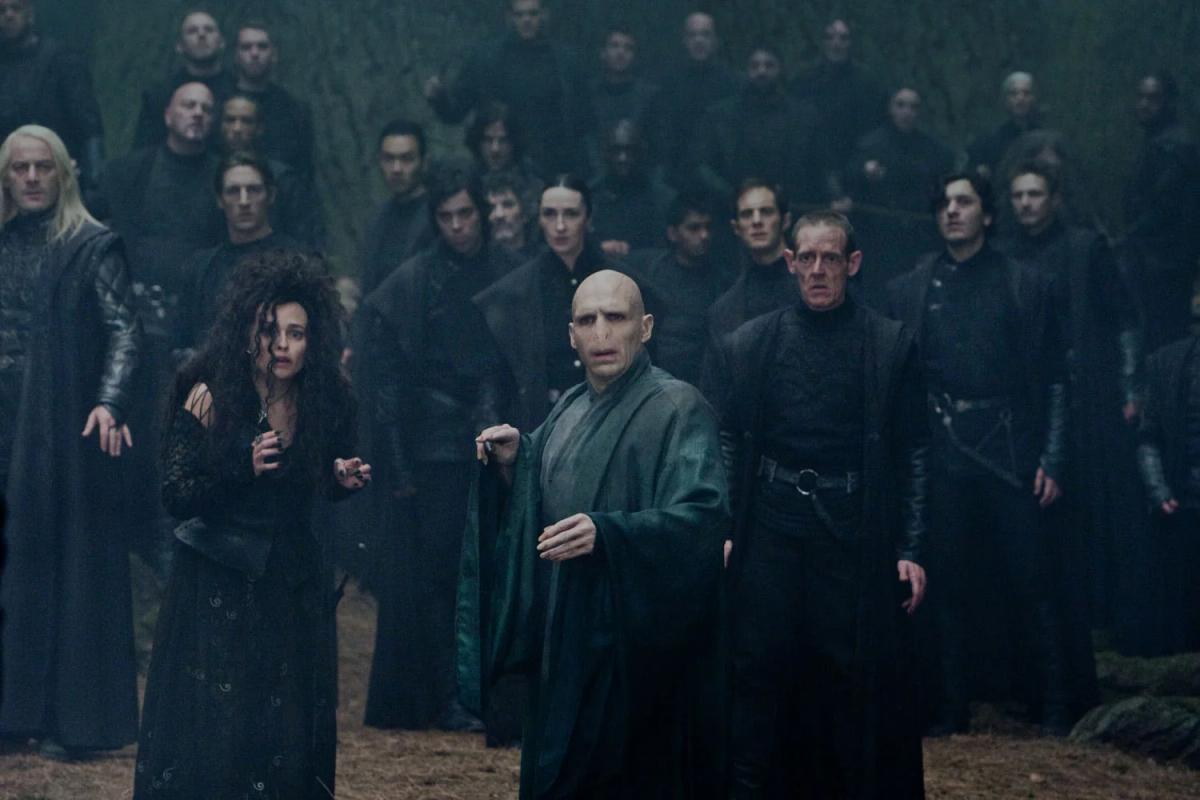 Ralph Fiennes as Lord Voldemort points his wand in the Forbidden Forest with Death Eaters behind him.