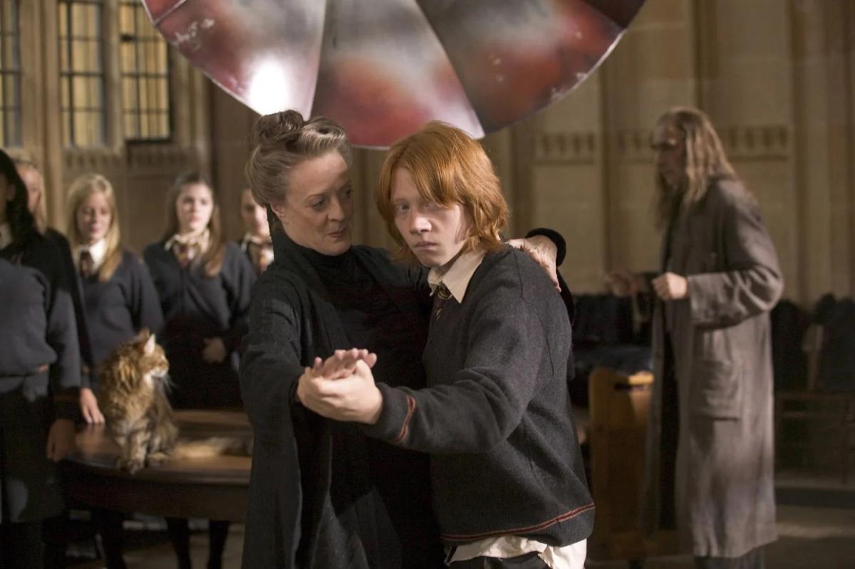 Maggie Smith as Minerva McGonagall waltzes with Rupert Grint as Ron Weasley while Gryffindor students watch.