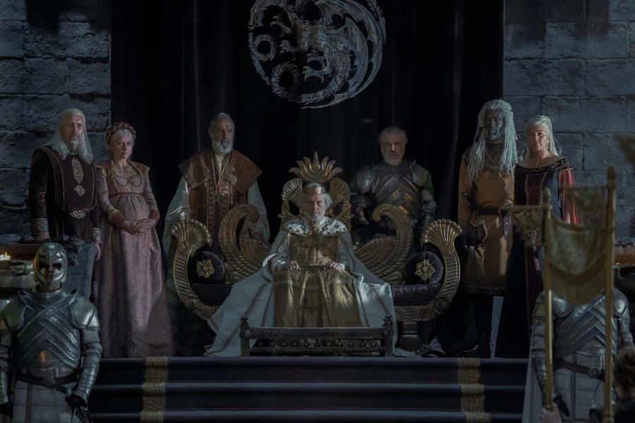 Michael Carter as an aged, crowned Jaehaerys I seated on a throne with courtiers standing on either side of him