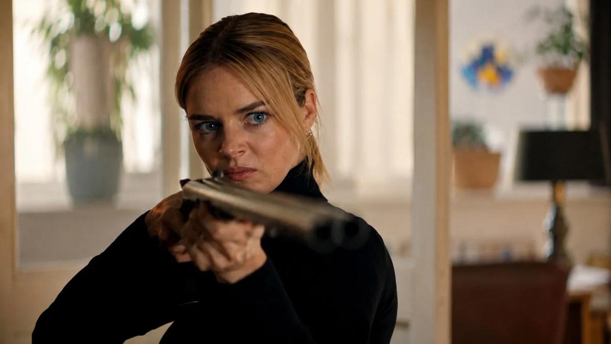 Samara Weaving as Lisa aiming a double-barrelled shotgun straight down the lens inside the cabin.