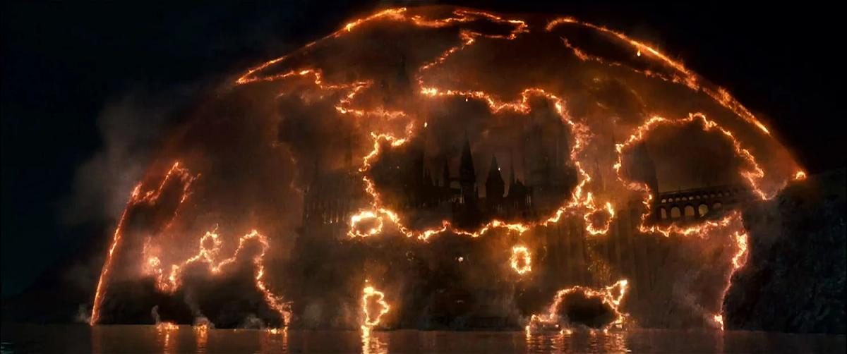 A vast dome of burning orange light breaking apart over Hogwarts castle at night.