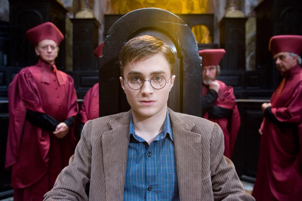 Harry Potter (Daniel Radcliffe) sits alone in a chair before rows of robed Wizengamot members during his Ministry hearing.