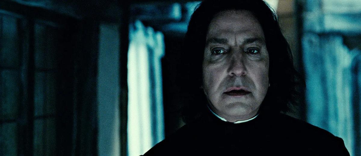Alan Rickman as Severus Snape kneeling beside Geraldine Somerville as Lily Potter in a wrecked room, holding her.