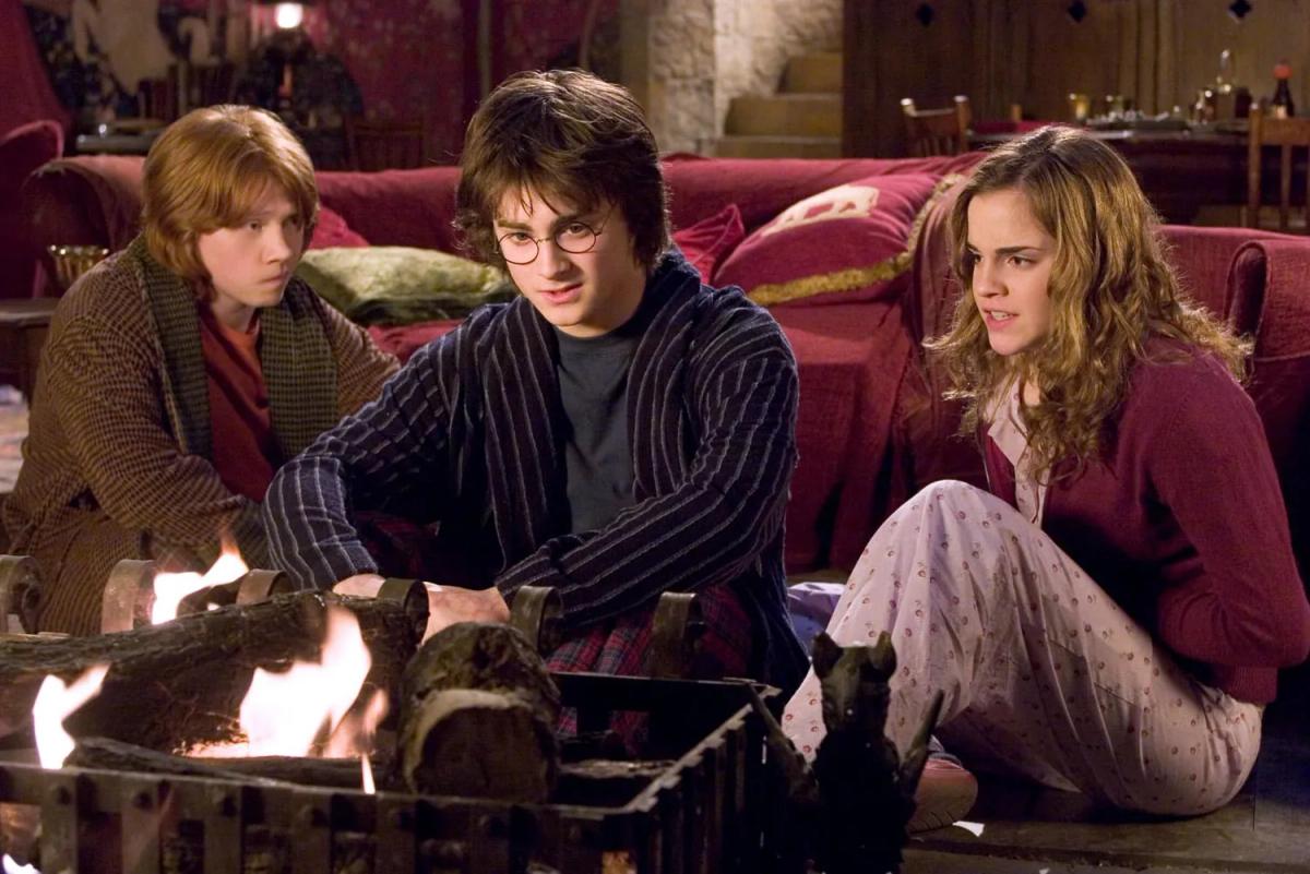 Rupert Grint as Ron Weasley, Daniel Radcliffe as Harry Potter and Emma Watson as Hermione Granger sit beside the fire in the Gryffindor common room.
