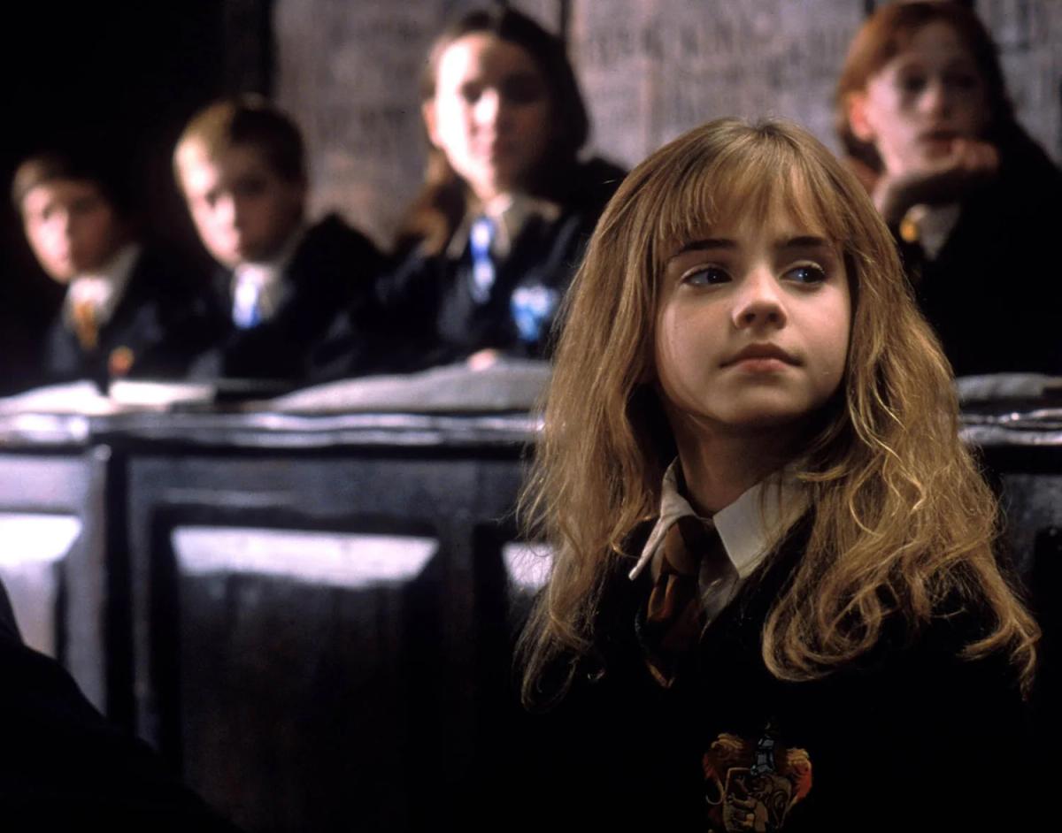 Emma Watson as Hermione Granger seated at a desk in a Hogwarts classroom