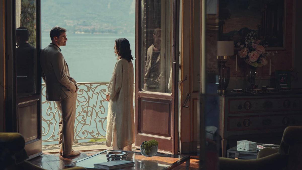 Theo James as Eddie Horniman and Benedetta Porcaroli as Bella at open balcony doors above an Italian lake.