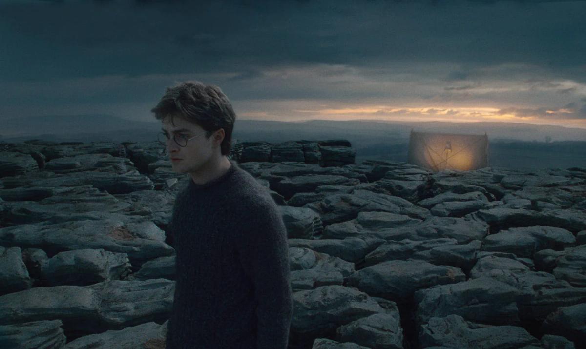 Harry Potter (Daniel Radcliffe) stands on a wide expanse of grey limestone with the tent a small shape on the horizon behind him.