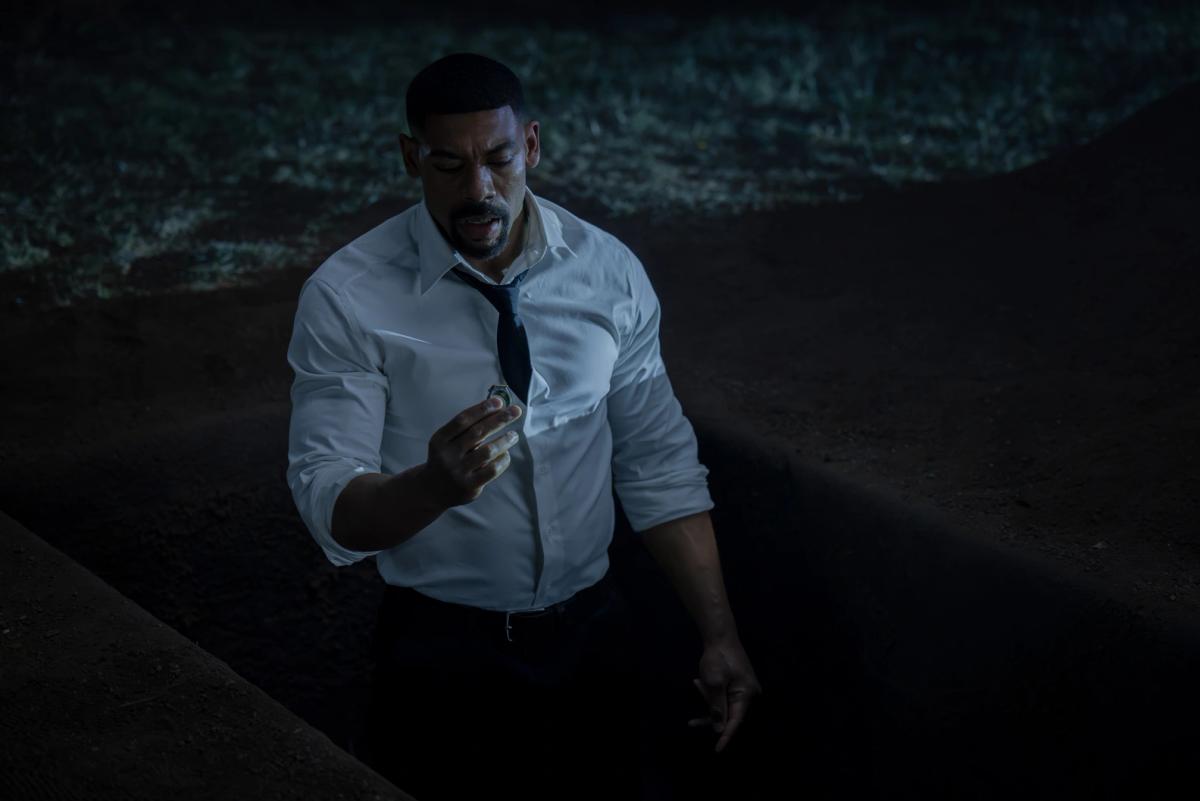 Aaron Pierre as John Stewart standing in an open grave at night, holding a ring up to the light.