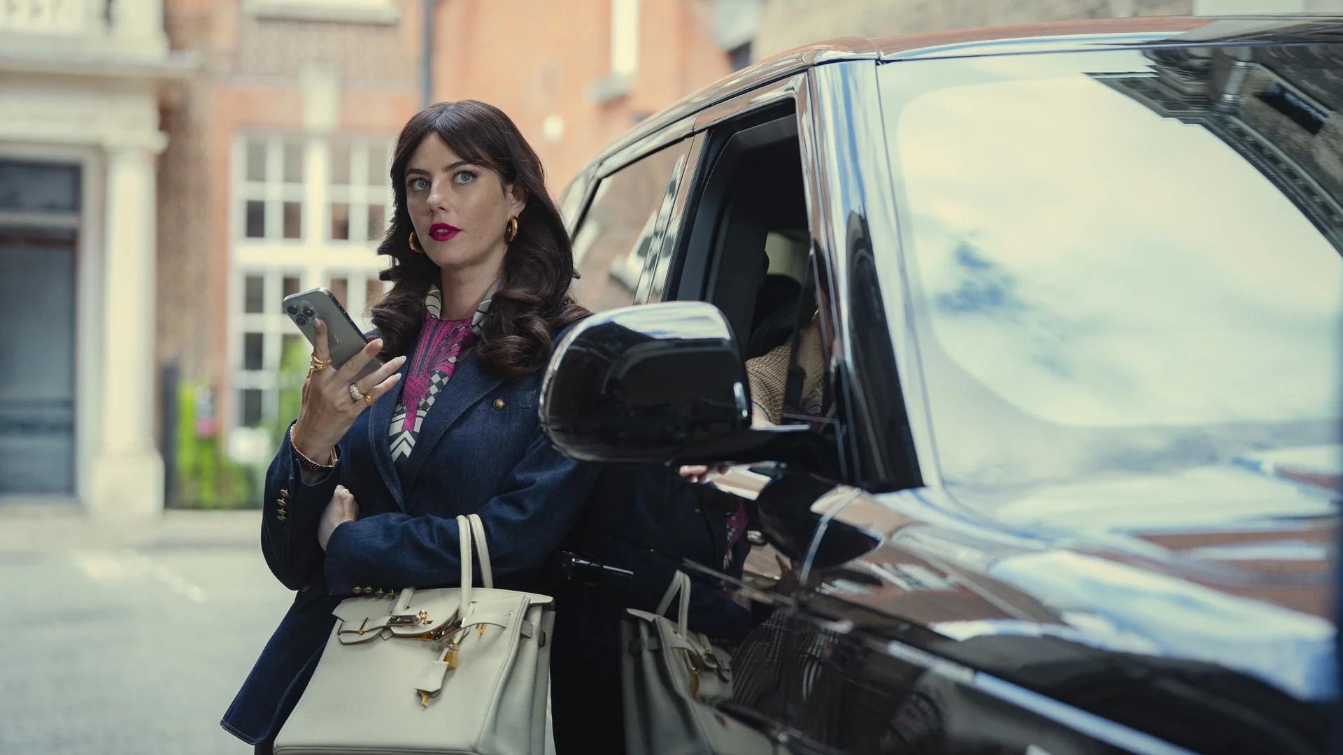 Kaya Scodelario as Susie Glass standing beside a black SUV with a phone in her hand, mid-call.