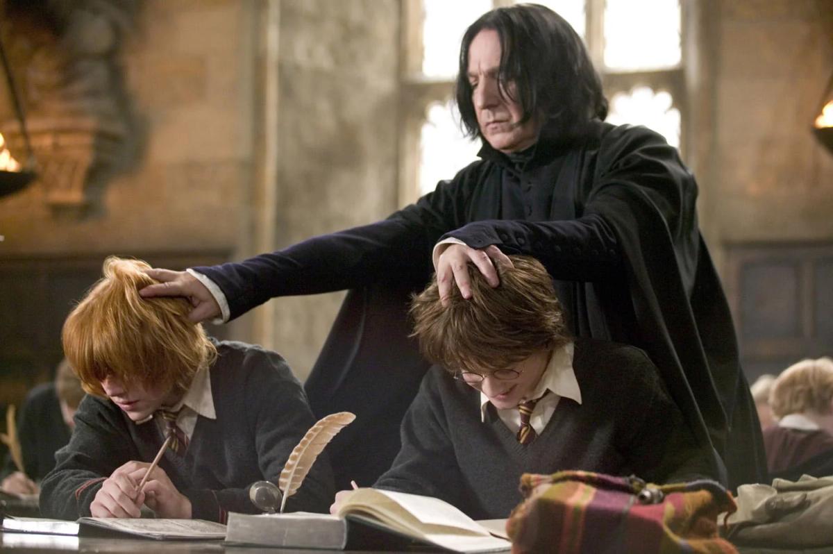 Alan Rickman as Severus Snape pushes the heads of Rupert Grint as Ron Weasley and Daniel Radcliffe as Harry Potter down towards their books during a study session.