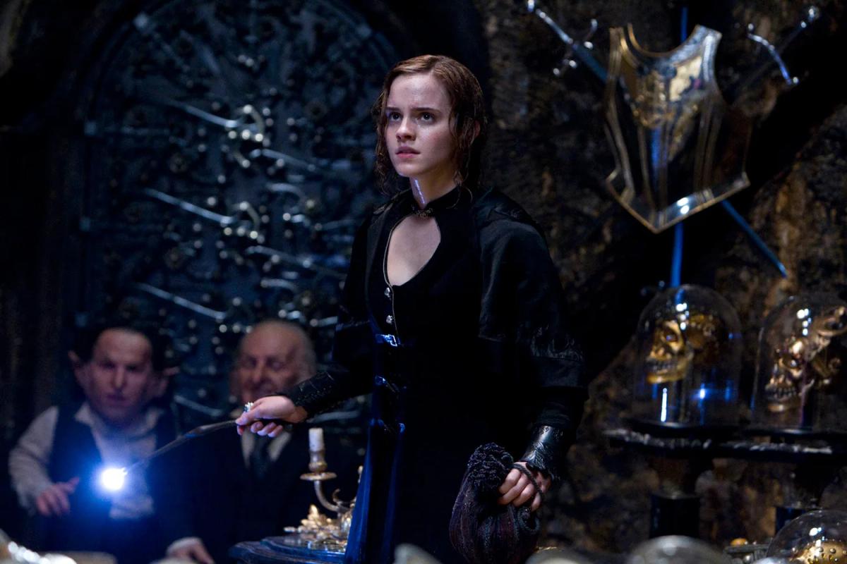 Emma Watson as Hermione Granger in Bellatrix Lestrange's black gown inside Gringotts, holding a wand as goblins and a wizard crowd around her.