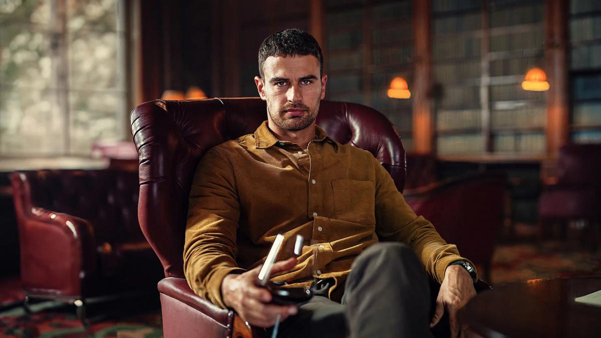 Theo James as Eddie Horniman, sitting alone in a leather armchair in the library at Halstead with a drink.