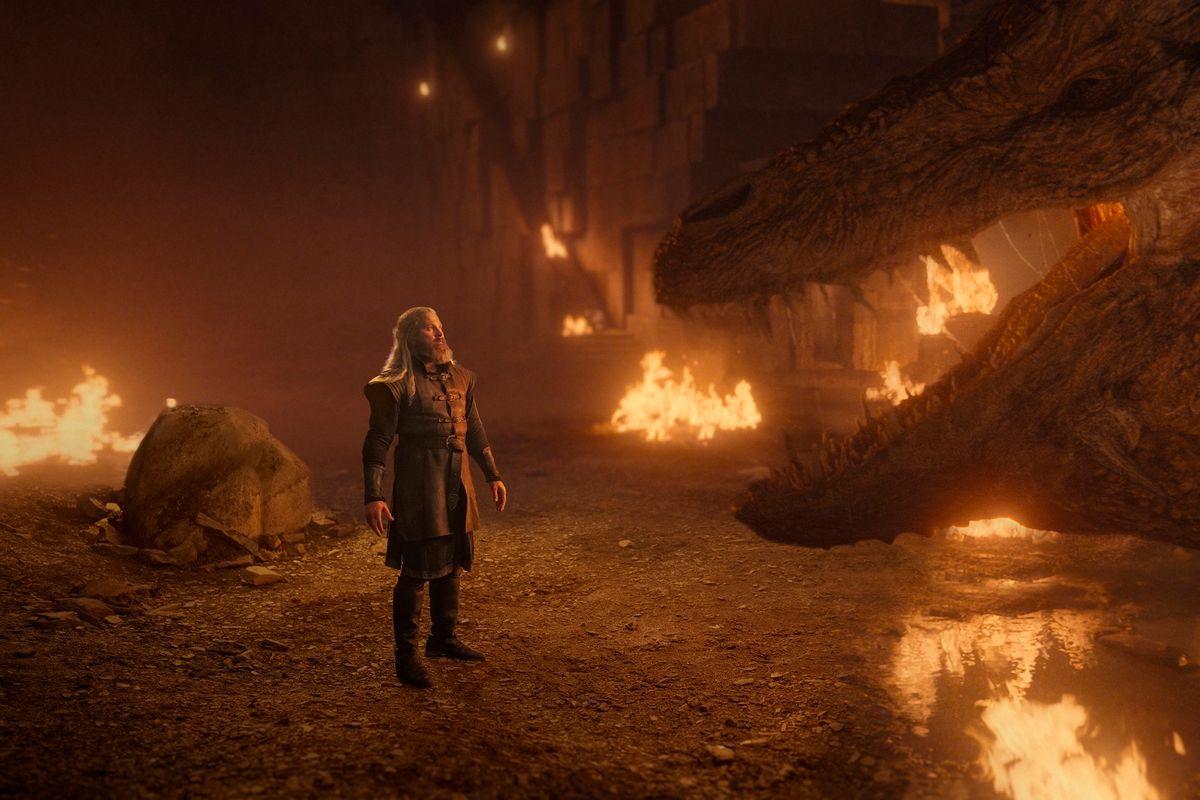 Hugh Hammer standing alone in the dragonmount facing Vermithor, fires burning across the cavern floor around them