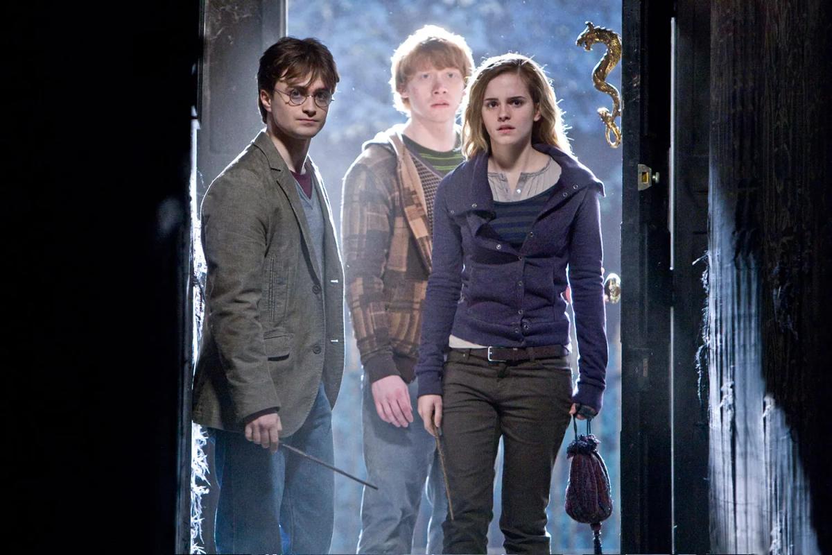 Daniel Radcliffe as Harry Potter, Rupert Grint as Ron Weasley and Emma Watson as Hermione Granger stand in the doorway of Grimmauld Place with their wands out.
