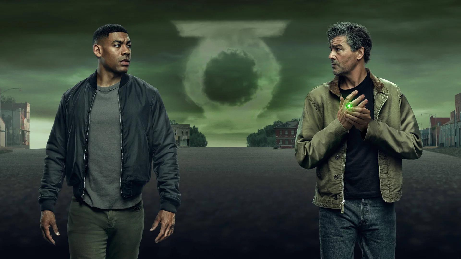 Aaron Pierre as John Stewart and Kyle Chandler as Hal Jordan standing at opposite ends of a Rushville street, a green Lantern symbol formed in the clouds behind them. Hal's ring glows on his hand.
