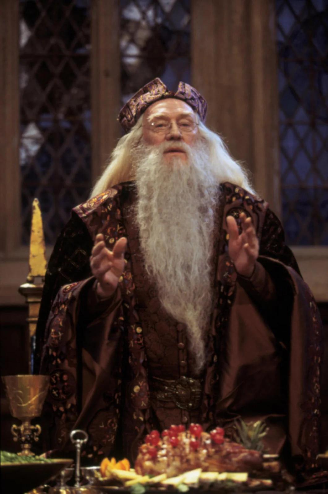 Albus Dumbledore (Richard Harris) addressing the school from the lectern in the Great Hall, hands raised.