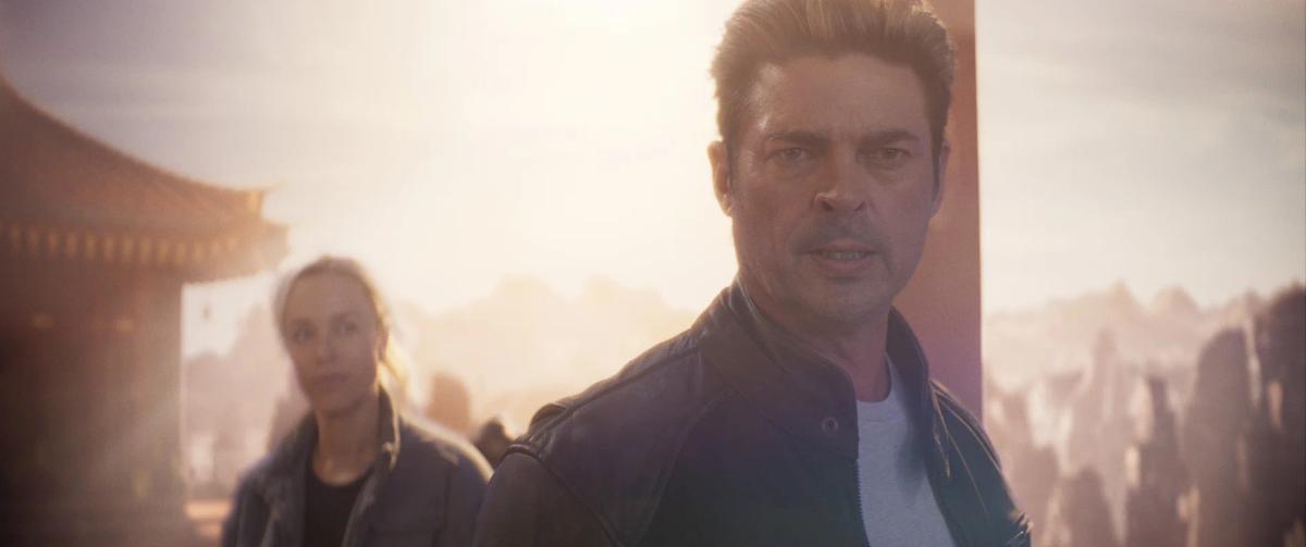 Karl Urban as Johnny Cage and Jessica McNamee as Sonya Blade standing in hazy sunlight beside a temple.