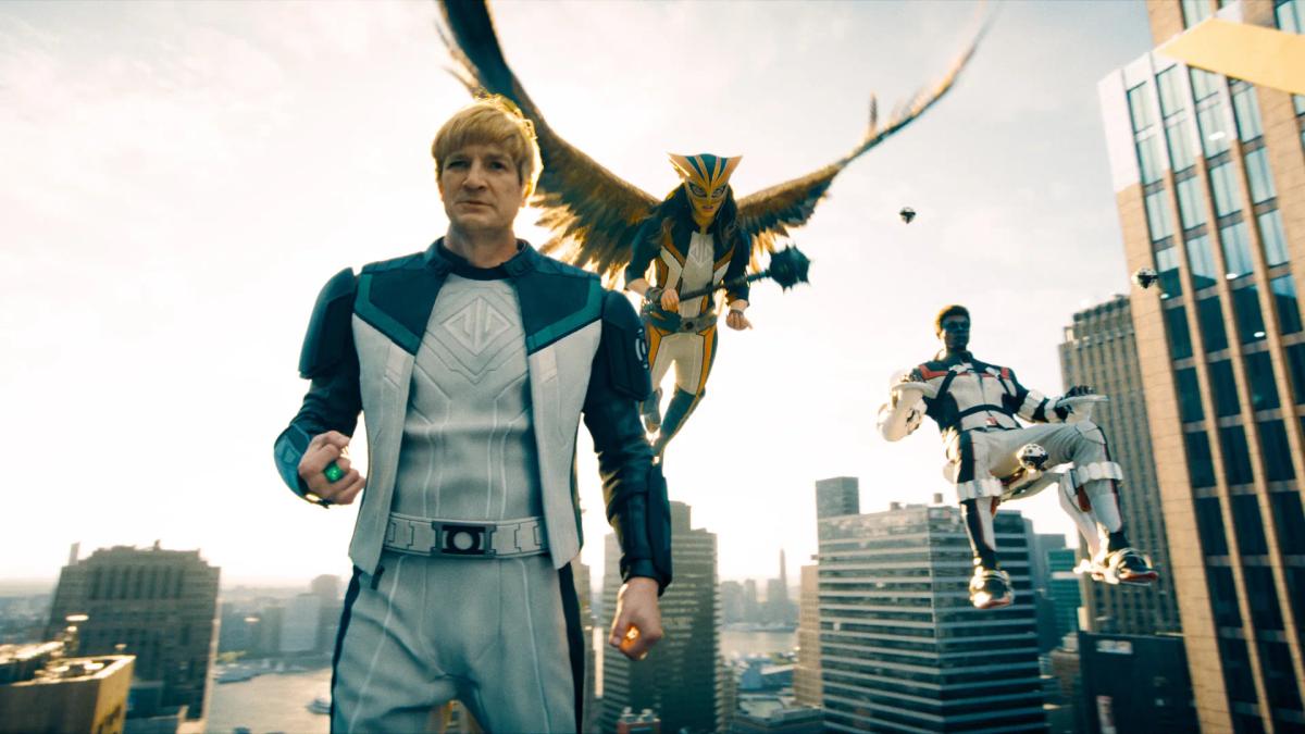 Nathan Fillion as Guy Gardner leading the Justice Gang across a rooftop in Superman, with Hawkgirl in flight behind him and Mister Terrific to his right.