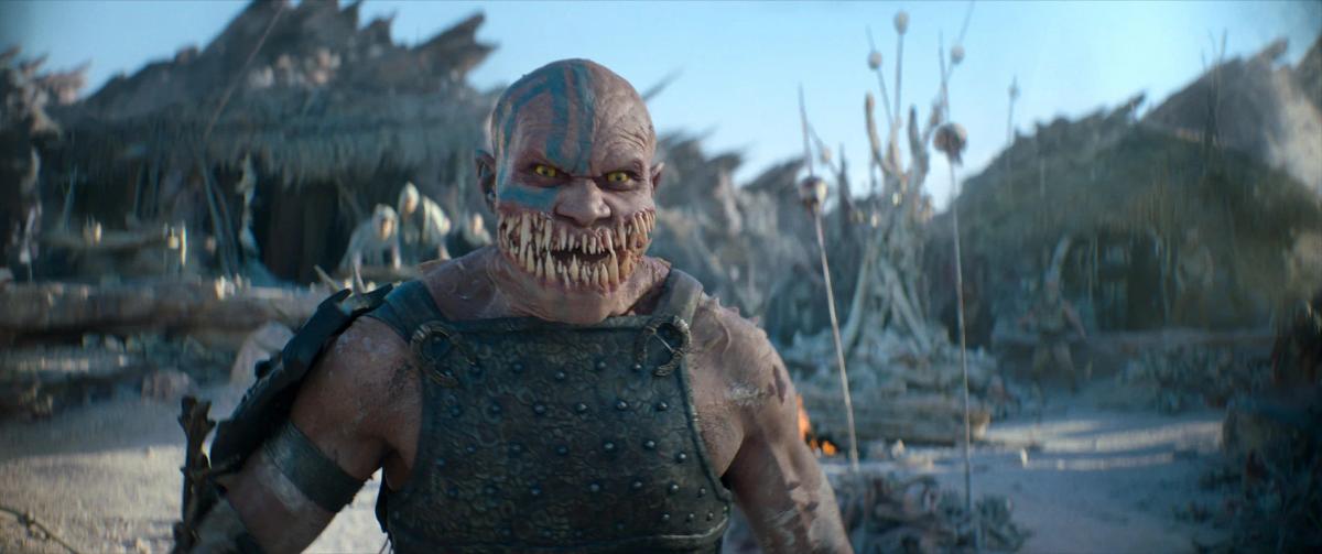 CJ Bloomfield as Baraka, his mouth full of jagged teeth, standing in a pale desert village.