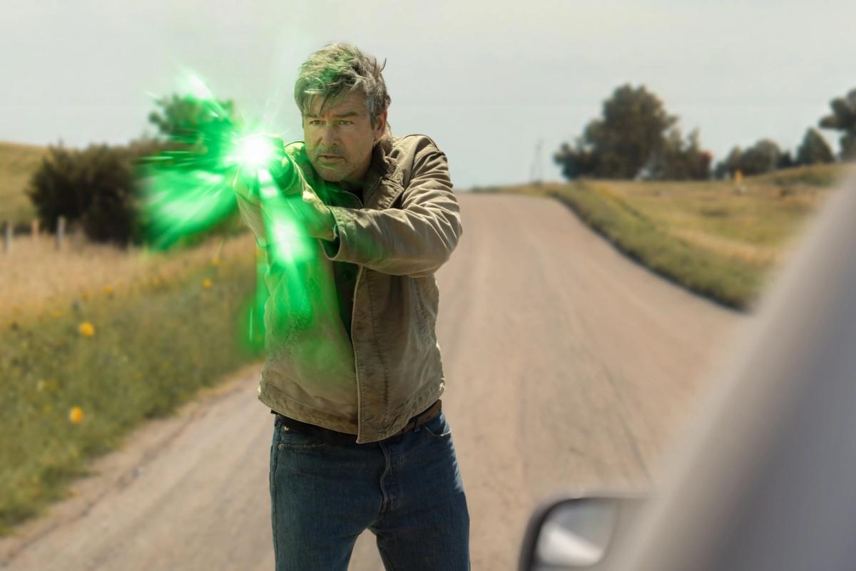 Kyle Chandler as Hal Jordan on a dirt road, firing a burst of green light from his power ring.