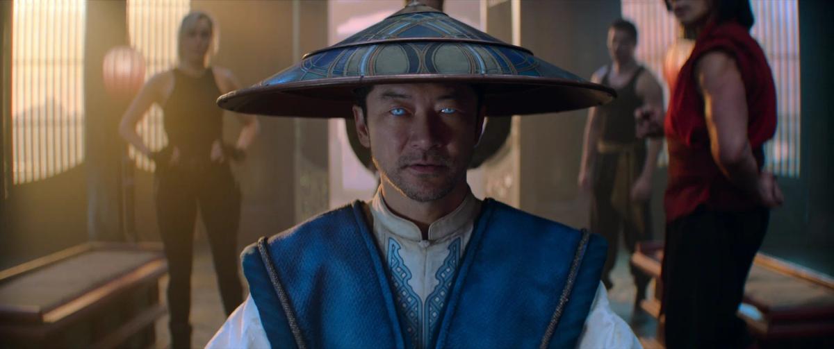 Tadanobu Asano as Raiden in his wide conical hat, with Jessica McNamee as Sonya Blade and Lewis Tan as Cole Young behind him in a sunlit hall.