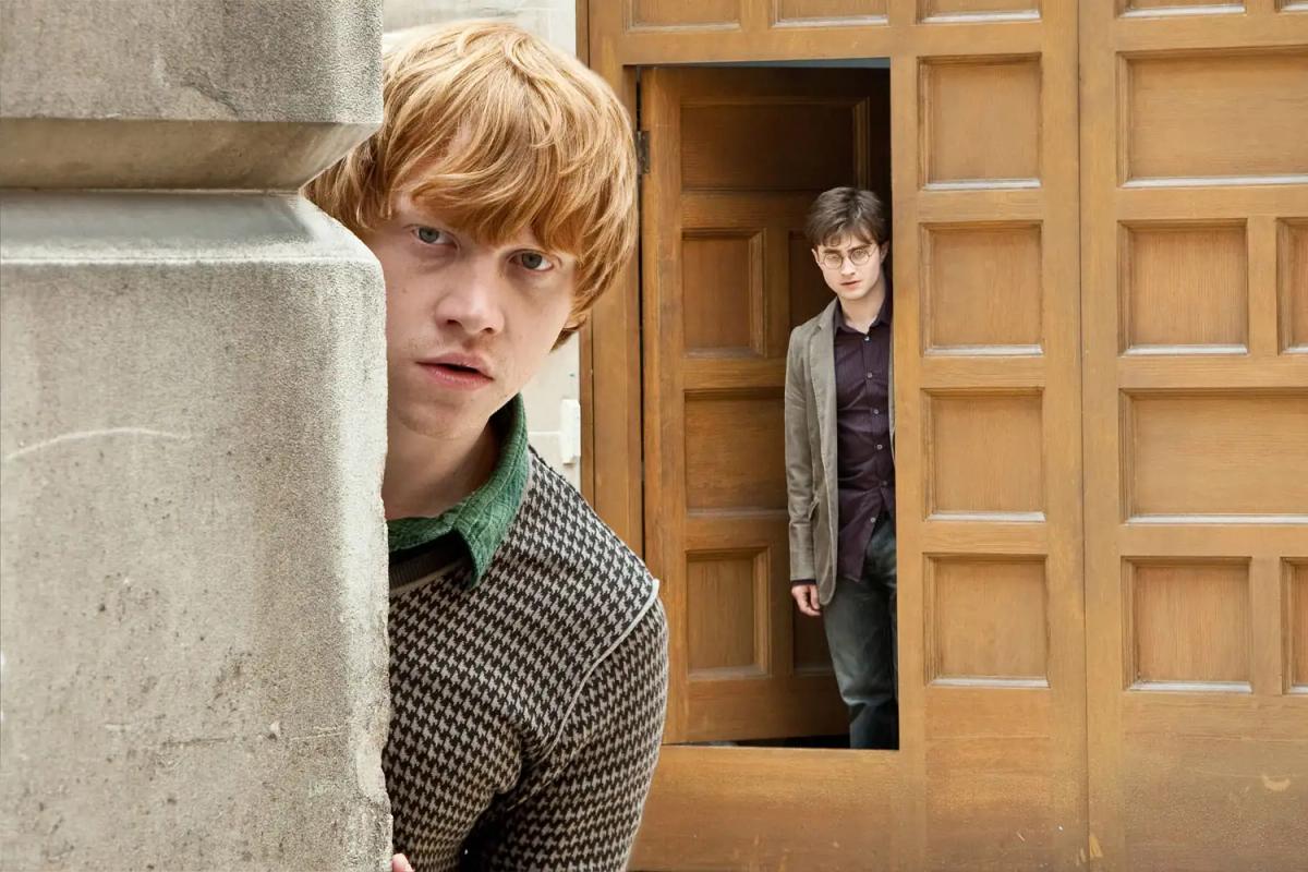 Ron Weasley (Rupert Grint) presses against a stone pillar while Harry Potter (Daniel Radcliffe) waits in a doorway behind him, both about to enter the Ministry.