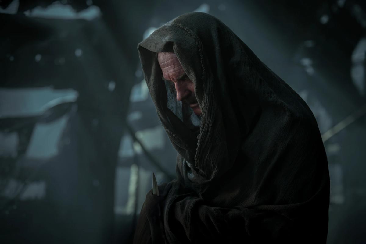 Ulrich Thomsen as Sinestro, hooded in rough cloth with a knife at his side, in a dark ruined interior.