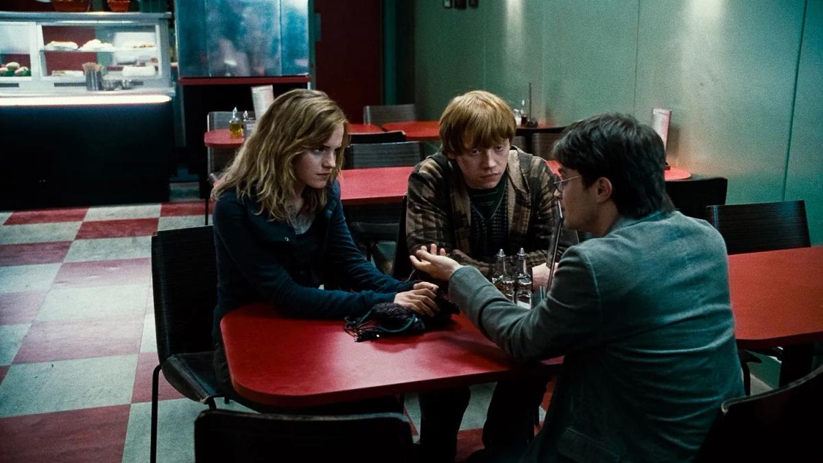 Emma Watson as Hermione Granger, Rupert Grint as Ron Weasley and Daniel Radcliffe as Harry Potter sit at a table in a café.