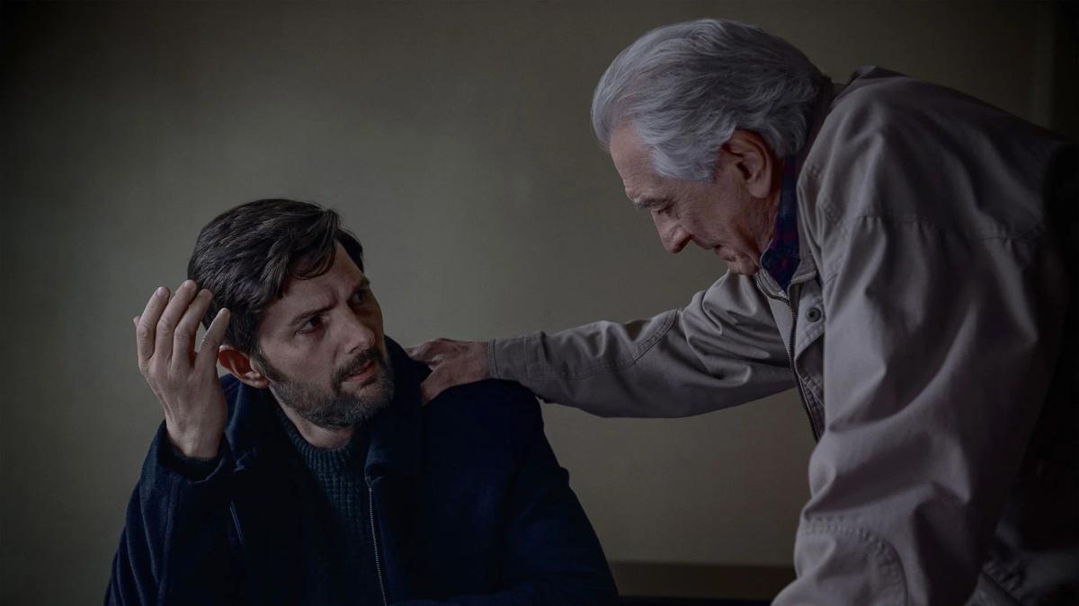 Robert De Niro as Pete Willis leaning over a seated Adam Scott as Tom Kennedy, one hand on his head.