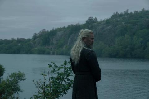 Hugh Hammer standing alone by a river in dark clothing, looking back over his shoulder