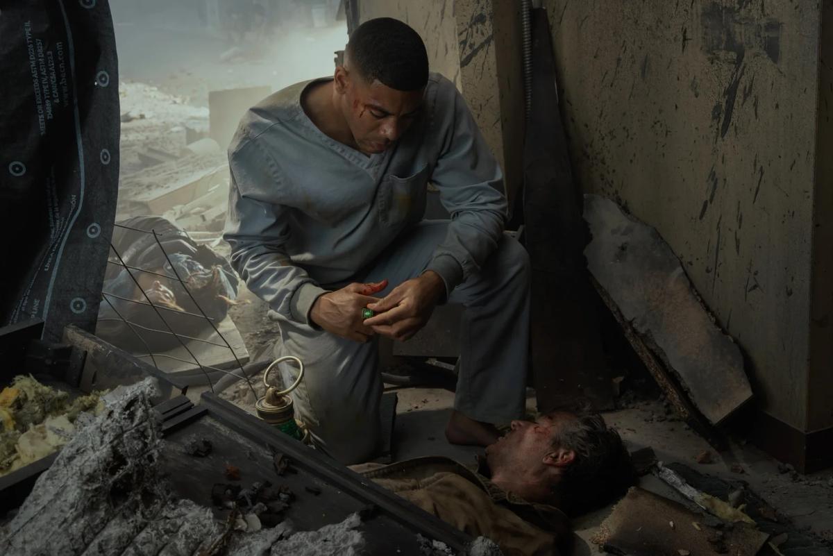 Aaron Pierre as John Stewart crouched in rubble in a hospital gown, holding a green power ring, with Kyle Chandler as Hal Jordan lying beside him.