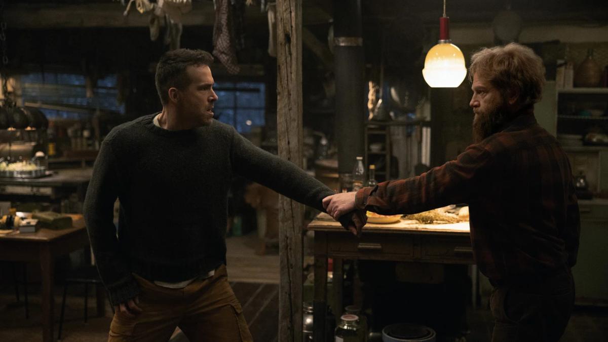 Kenneth Branagh as Nikolai Ustinov reaching out to Ryan Reynolds as Troy Kelly across his cluttered workshop