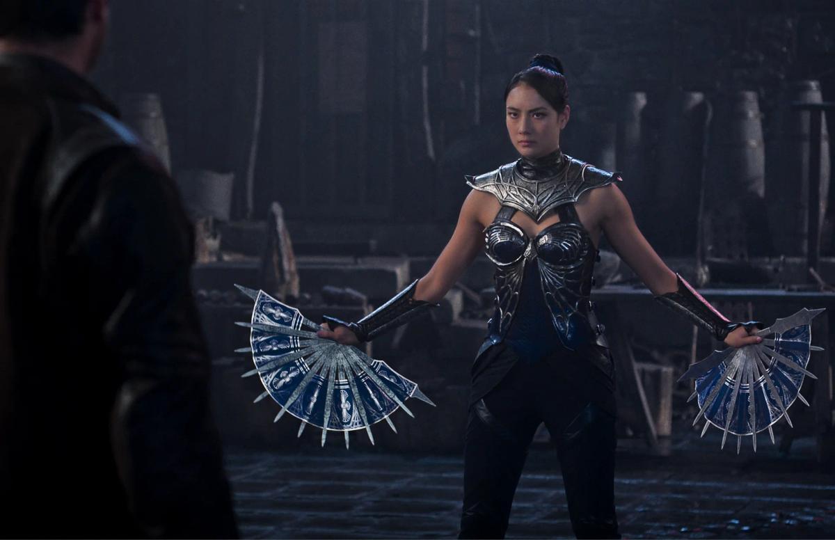 Adeline Rudolph as Kitana in silver armour, holding her bladed steel fans open at her sides.