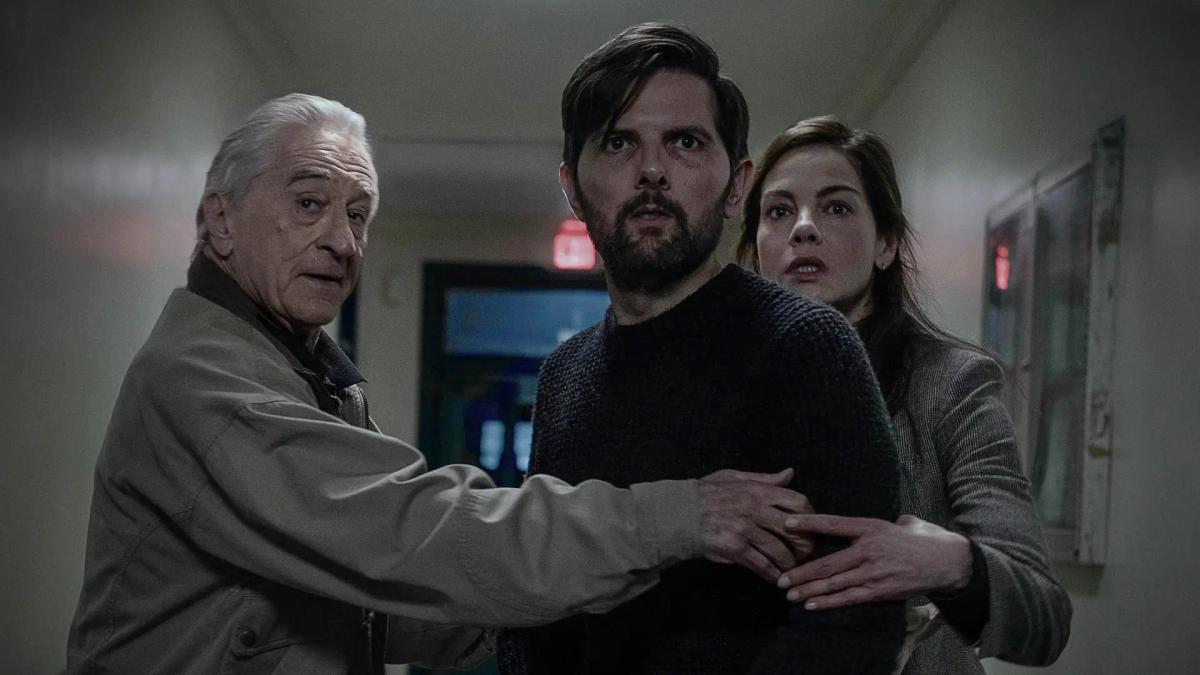 Adam Scott as Tom Kennedy standing with Acston Luca Porto as Jake outside a school, beside a noticeboard carrying a missing child poster.