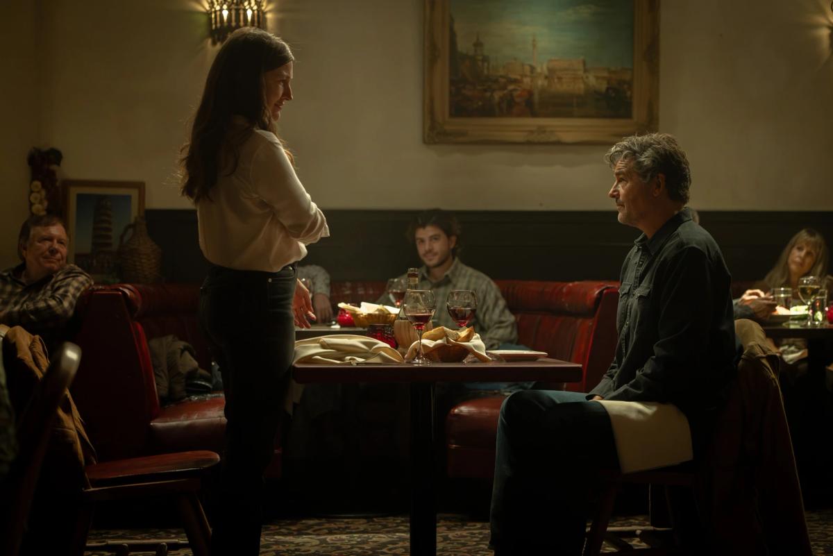 Kelly Macdonald as Kerry Kane standing beside a restaurant table and speaking to Kyle Chandler as Hal Jordan, who is seated, while other diners watch from the booths.
