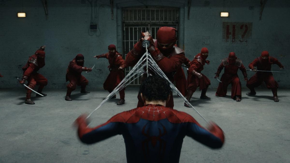 Spider-Man seen from behind, arms spread, firing webs at nine masked fighters in red who surround him in a concrete corridor