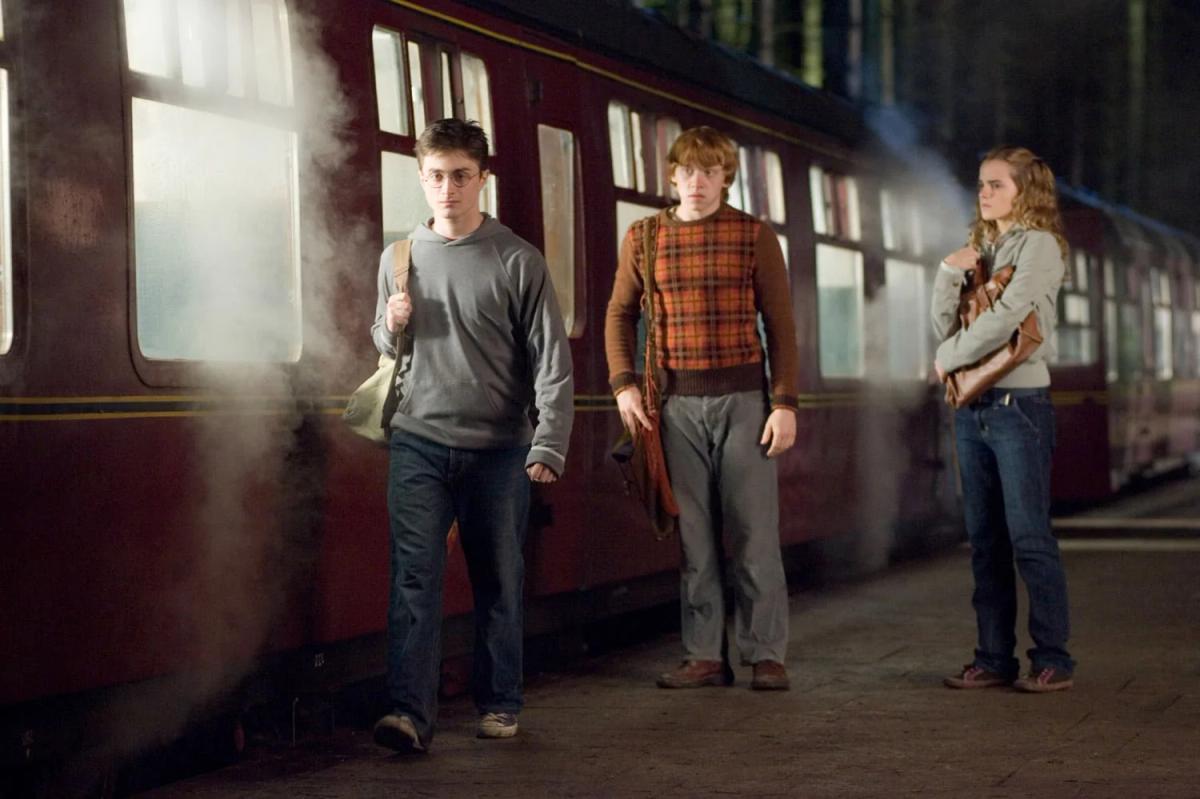 Daniel Radcliffe as Harry Potter, Rupert Grint as Ron Weasley and Emma Watson as Hermione Granger stand beside the Hogwarts Express.