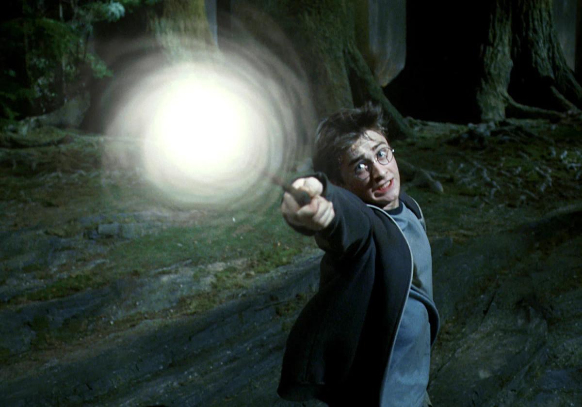 Daniel Radcliffe as Harry Potter casting the Patronus Charm in a dark forest, a ball of white light spreading from the end of his wand.