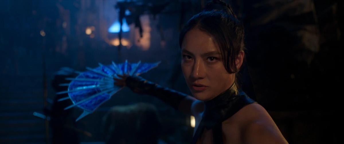 Adeline Rudolph as Kitana, holding a glowing blue fan in the dark.