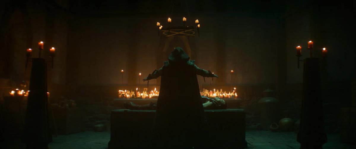 Damon Herriman as Quan Chi and Max Huang as Kung Lao in a dim chamber lit by rows of candles.